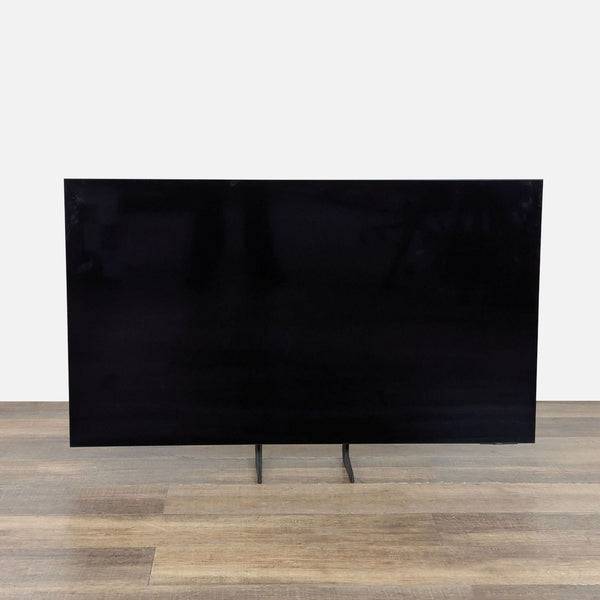 Front view of a 55-inch Samsung OLED 4K Smart TV with slim bezels and a modern stand on wood flooring.  