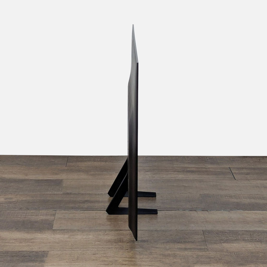 Side profile of an ultra-thin Samsung OLED 4K Smart TV showing its Contour Design on a wooden floor background.