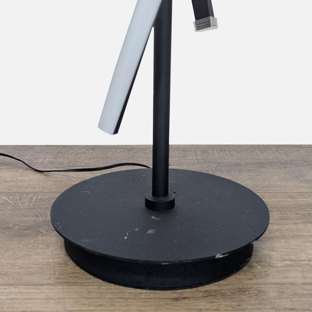 Base detail of a black metal spiral floor lamp with LED, showing the round stand and cord from Reperch.