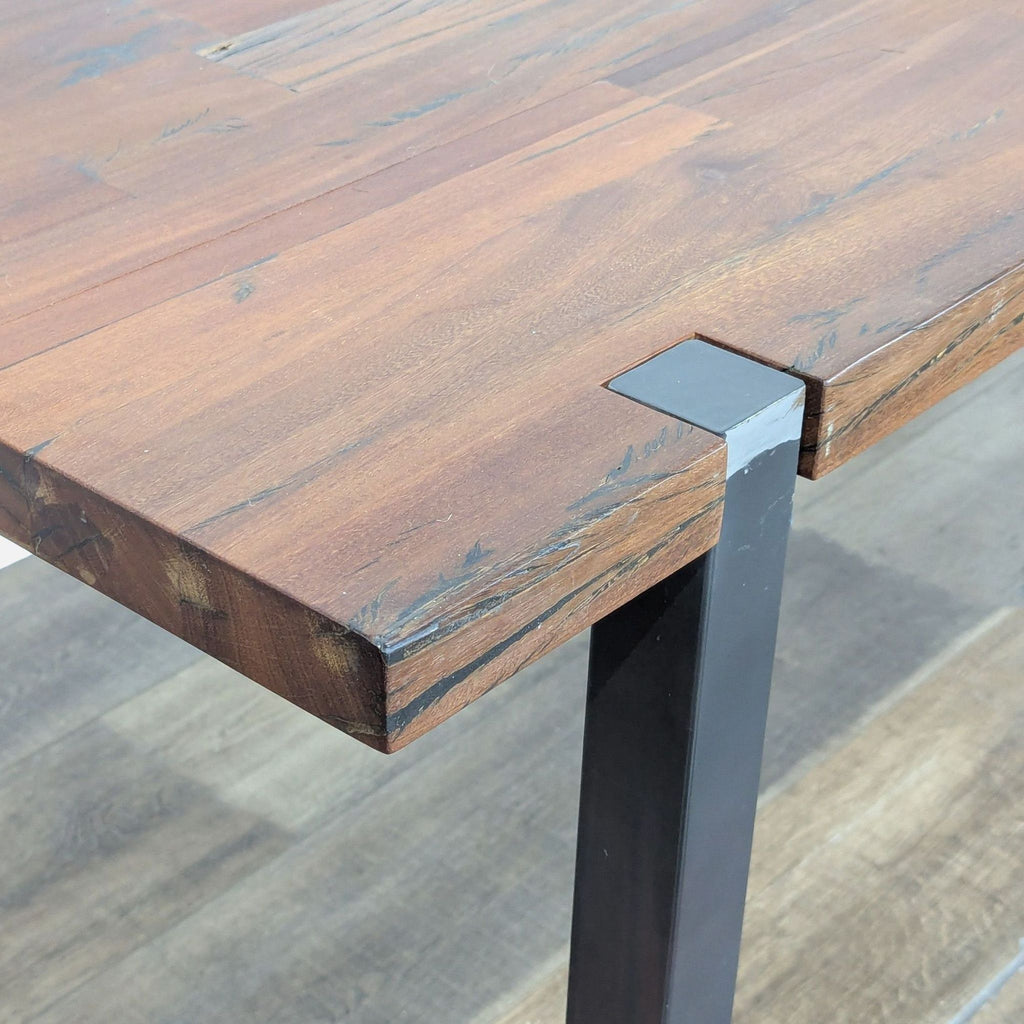 3. Detailed view of CB2 dining table edge highlighting wood texture and industrial metal corner leg.