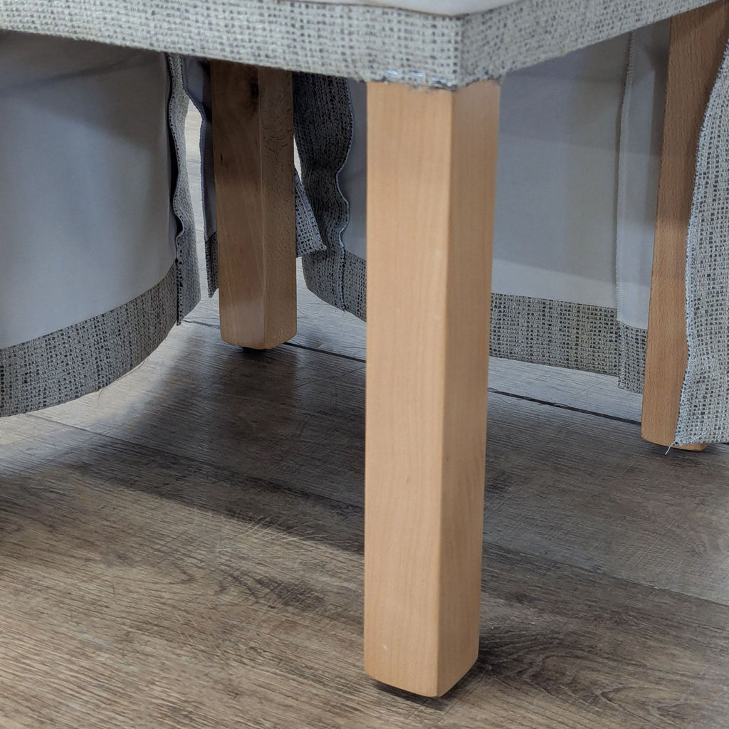 3. Bottom view of Reperch ottoman, showing wood legs and fabric skirt partially raised above the floor.