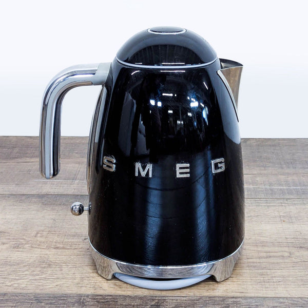Smeg Retro Style Electric Kettle in glossy black with chrome accents, viewed from the front on a wooden surface.  