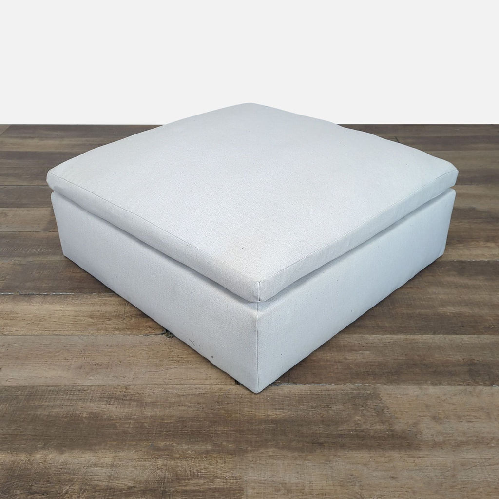 1. Reperch ottoman with a square, light-colored cushion and minimalist design on wooden floor.  