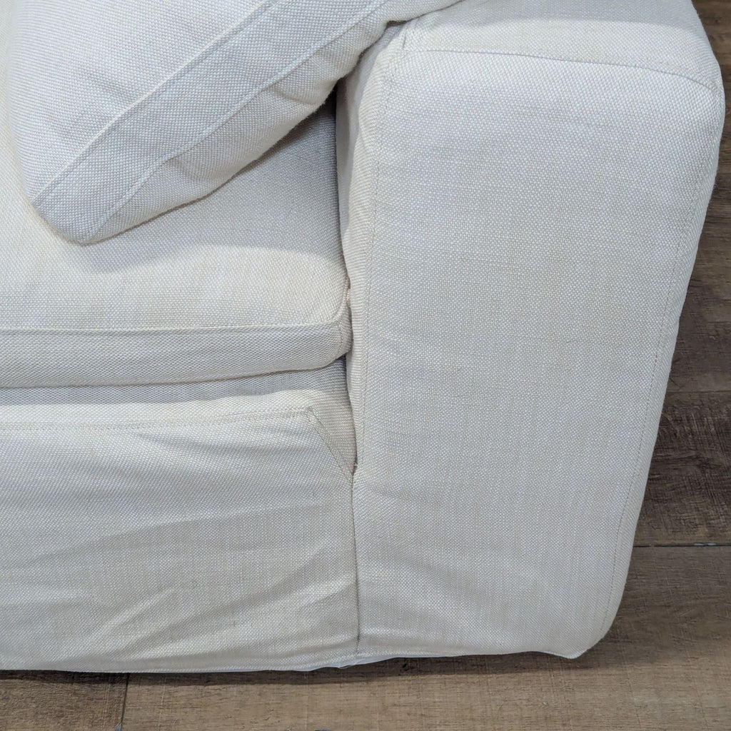 3. Detailed view of the sectional's wide, padded track arm and textured fabric upholstery on wooden floor.