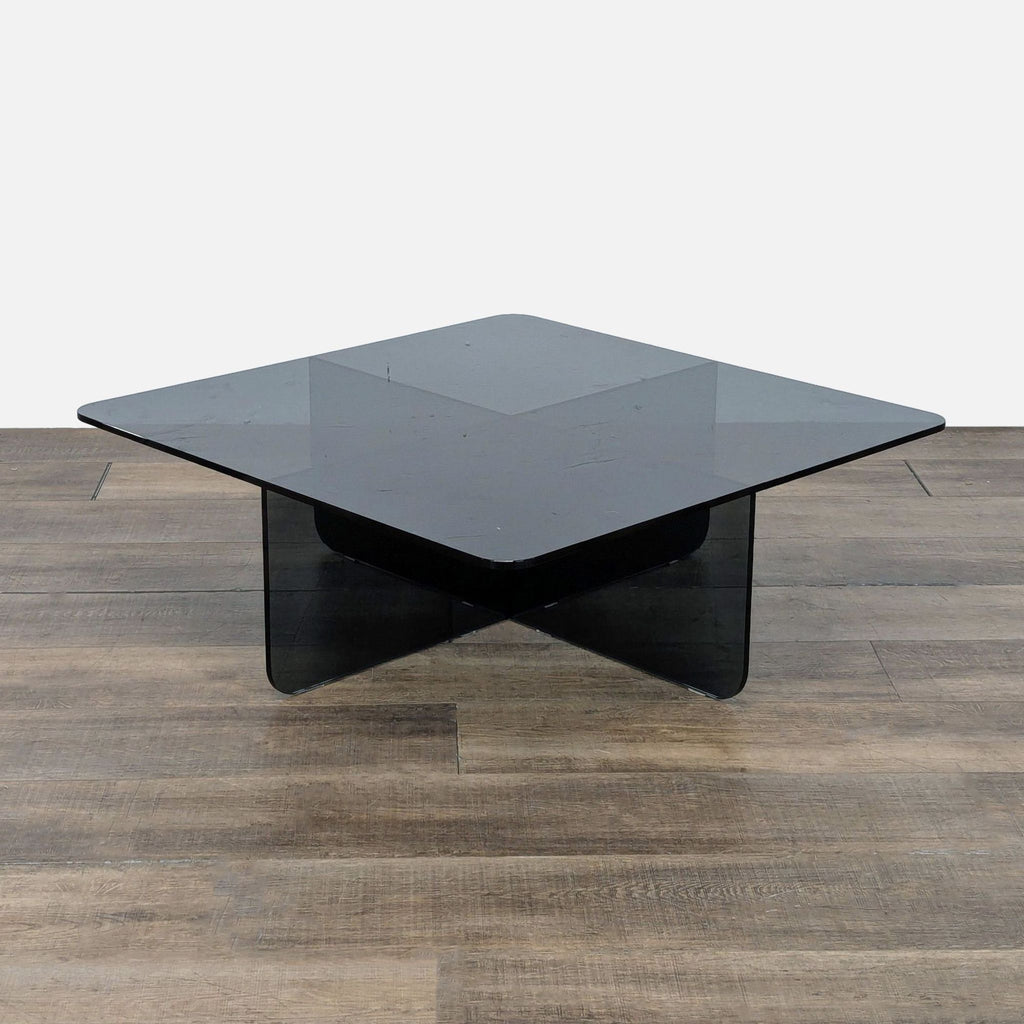 3. Angled shot of an EQ3 square coffee table featuring a black tempered glass top and modern crisscross base.