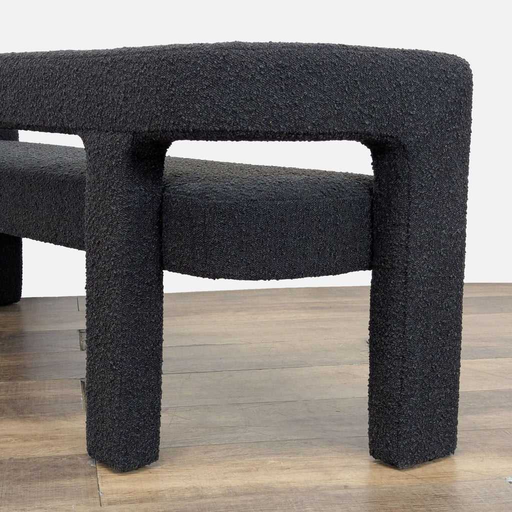 3. Side angle of CB2 black boucle bench leg and backrest, highlighting curved, padded design and unique shape.