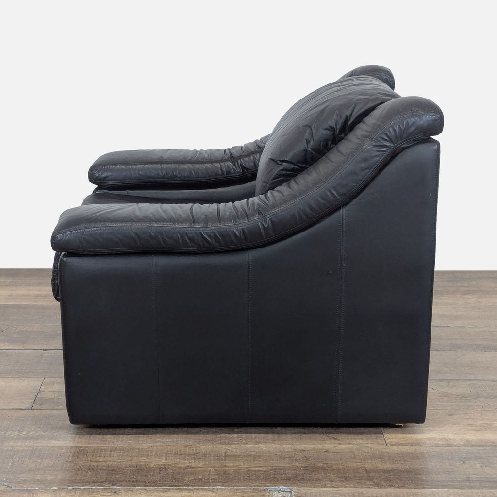 2. Side profile of a black leather lounge armchair by Krause’s Sofa Factory, showing thick cushioned arms.  