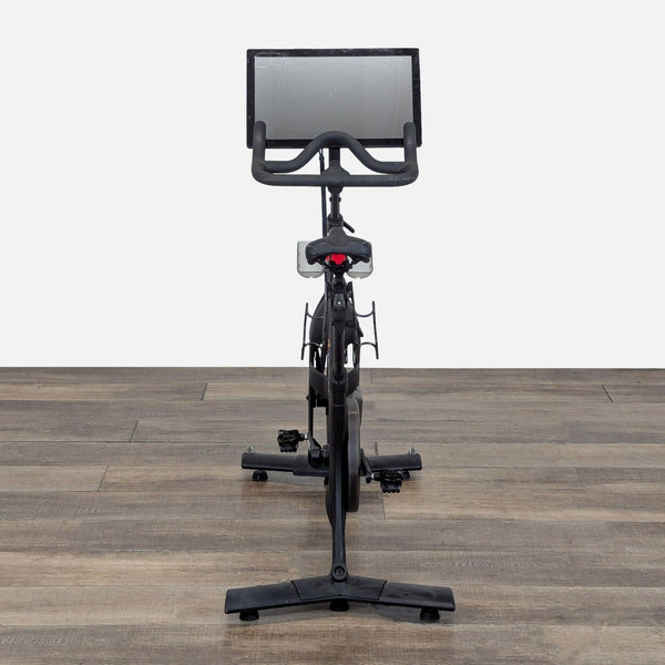 Front view of a Peloton Bike PLTN-RB1VQ with large touchscreen, on a wood floor, for home cardio workouts.  
