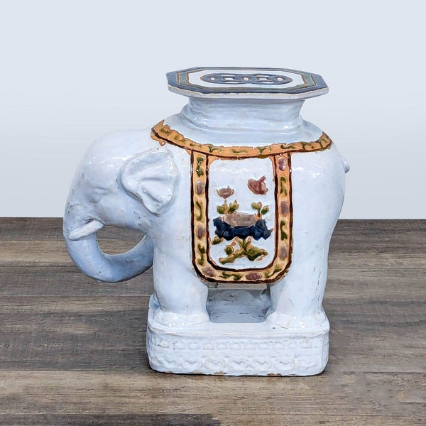 1. White ceramic elephant stool by Reperch, with floral and gold accents, viewed from the left side.