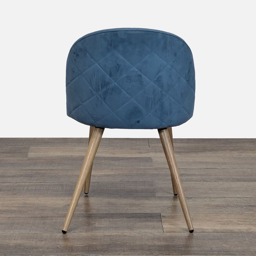 Back view of a Reperch dining chair showing quilted blue velvet upholstery and wooden legs.