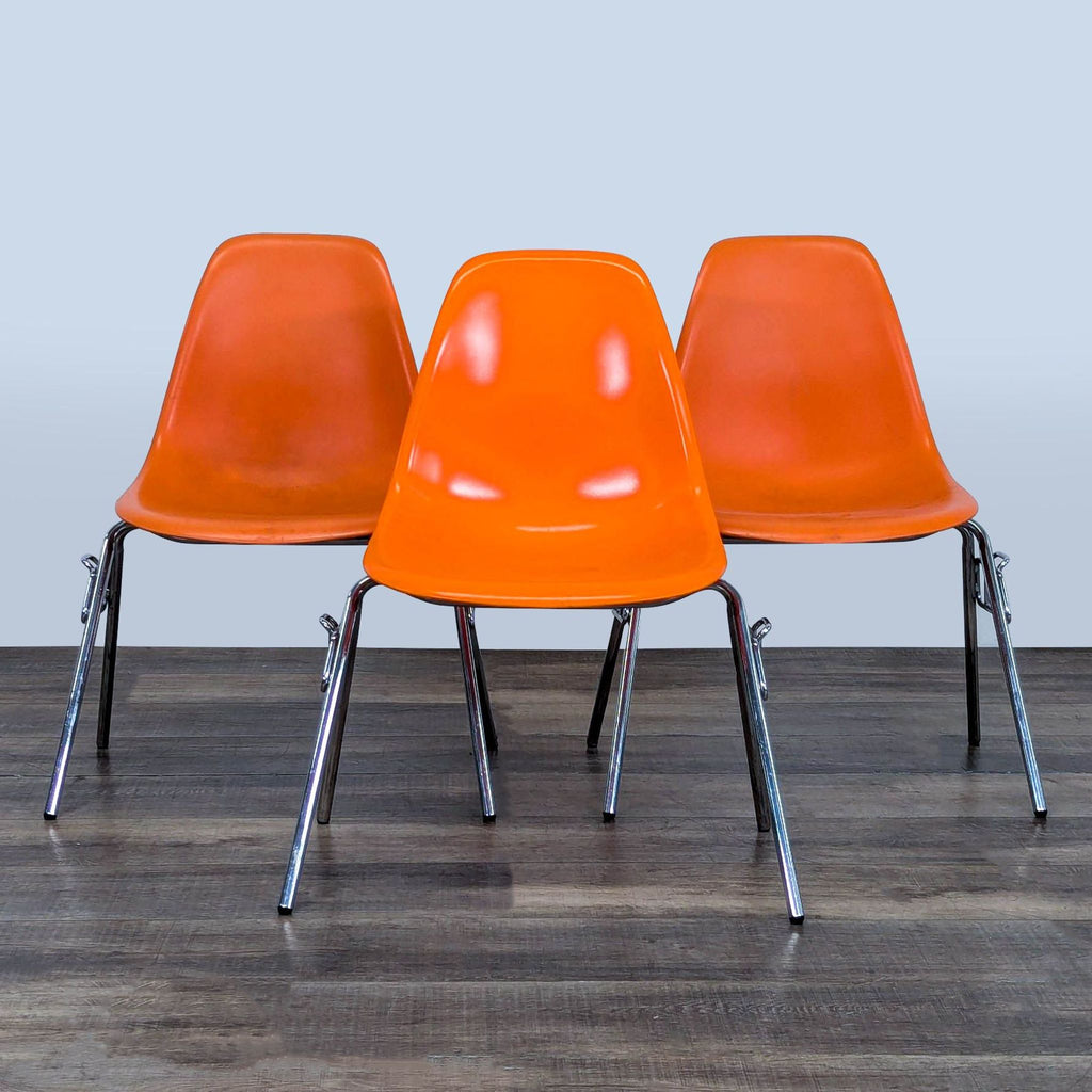 Three orange Reperch chairs with plastic seats and chrome legs, grouped together on wooden floor.