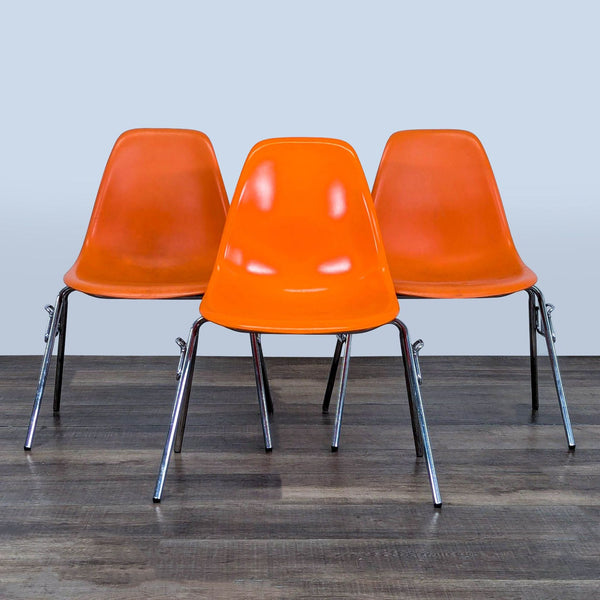 Three orange Reperch chairs with plastic seats and chrome legs, grouped together on wooden floor.