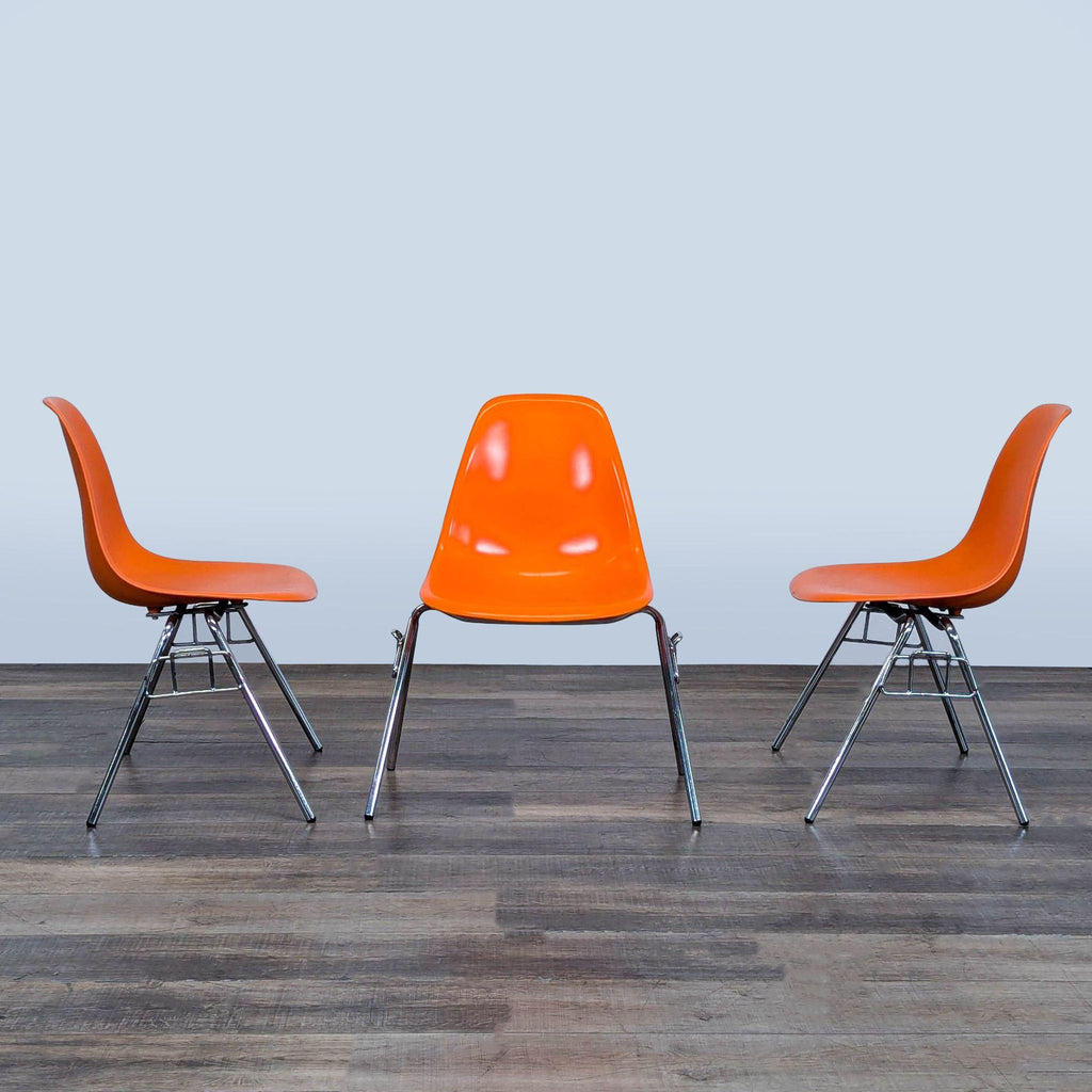 Set of three Reperch brand orange chairs with durable plastic seats and shiny chrome legs on display.