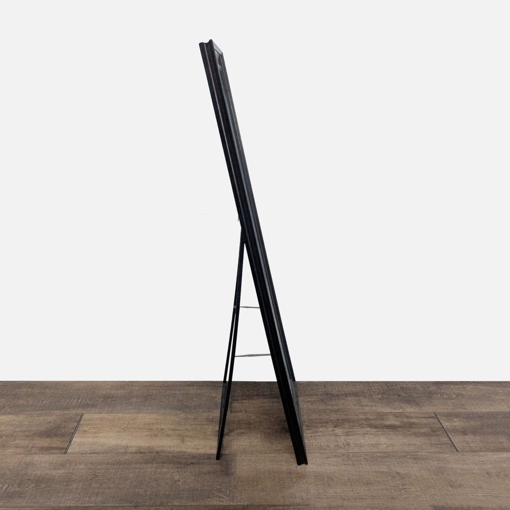 Side view of a Target floor mirror with a slim dark frame and support stand, placed on wood flooring.  