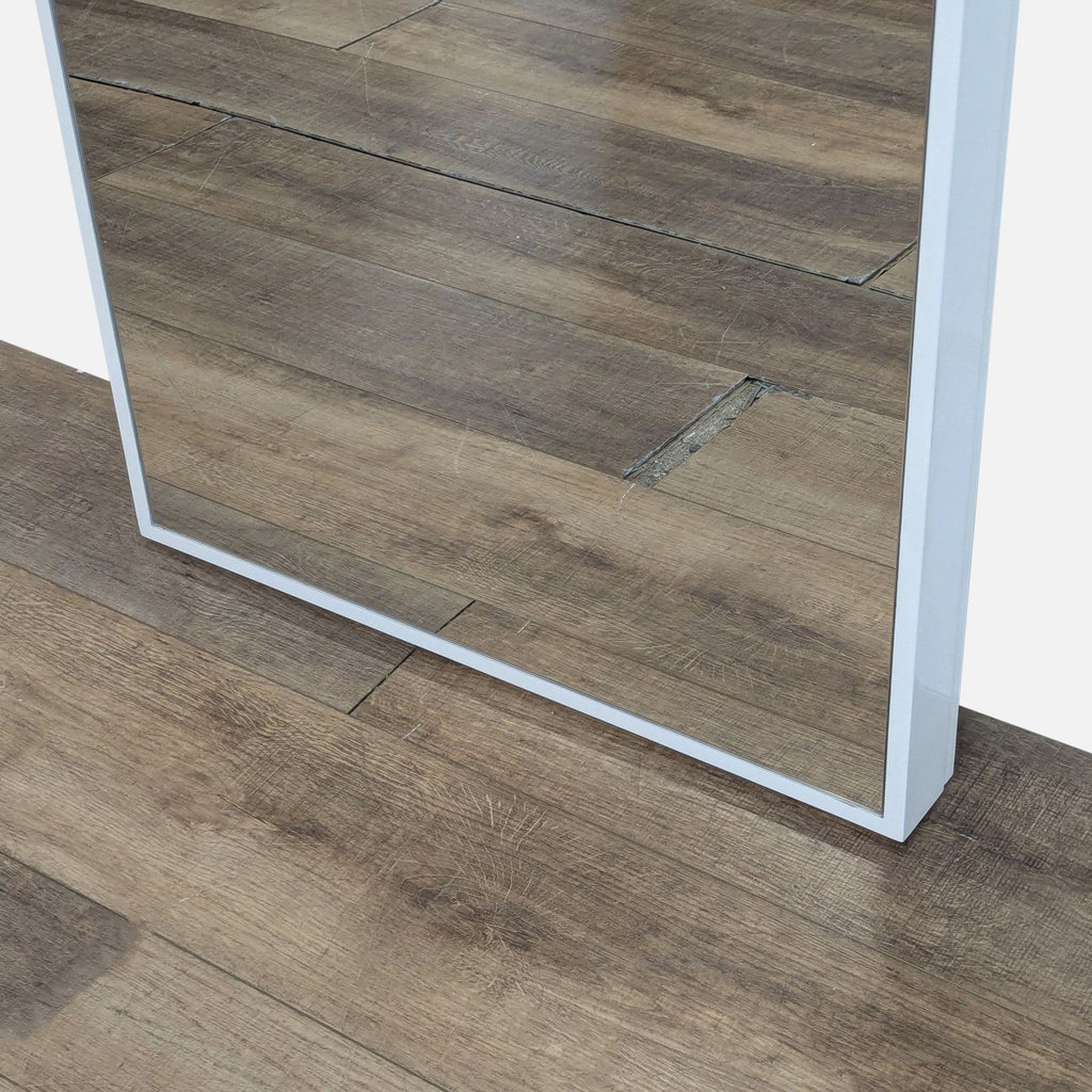 3. Close-up of the bottom corner of the Reperch mirror with white frame on a wooden floor.