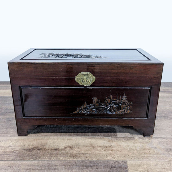 1. Dark wood Reperch trunk featuring carved scenic designs and brass clasp, displayed on a wooden floor.