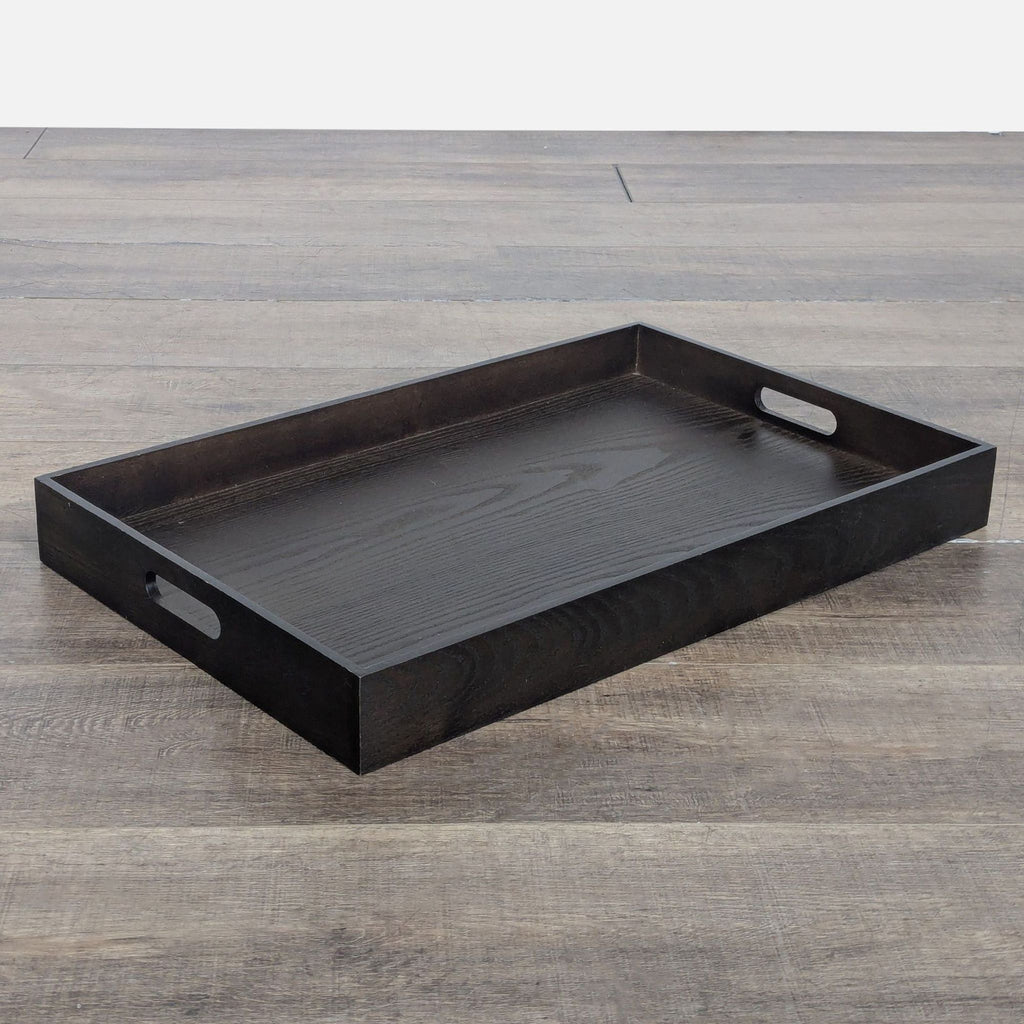1. Rectangular dark wood serving tray from West Elm with cutout handles, shown on a wooden floor, angled view.