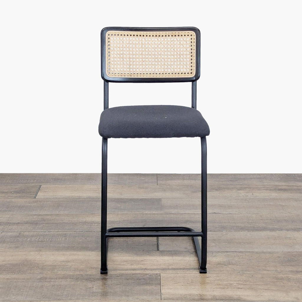 Front view of a Reperch stool with a black metal frame, upholstered seat, and woven rattan backrest.