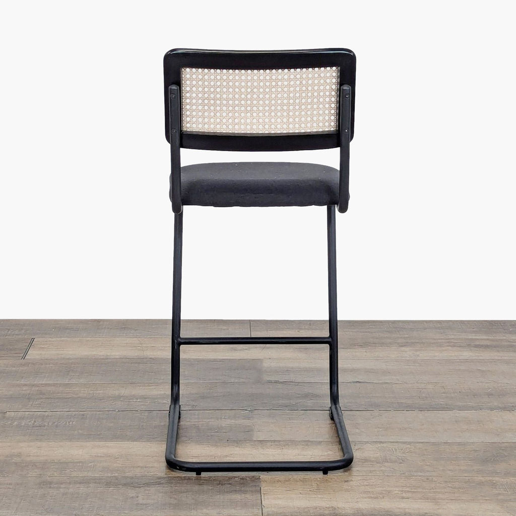 Rear view of a Reperch stool showing its black metal frame, cushioned seat, and woven rattan back detail.