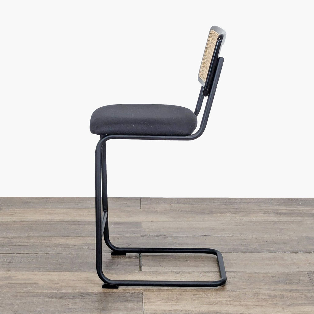 Side view of a Reperch stool featuring a cantilevered black metal frame and cushioned seat with rattan back.