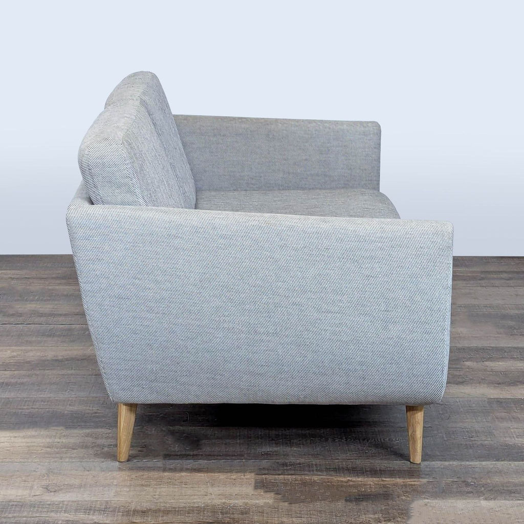 2. Side profile of a grey Ikea loveseat showing armrest, wooden legs, and fabric cushion details.