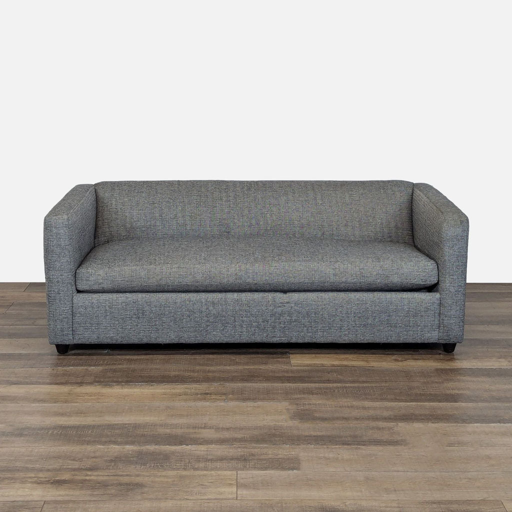 1. Grey CB2 sleeper sofa with deep single cushion seat, shown on a wood floor against a plain background.