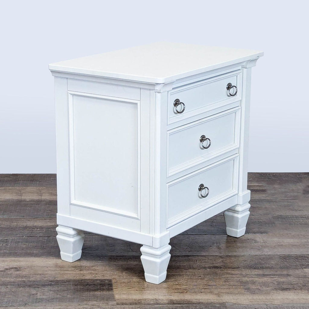 3. Angled view of white Ashley end table featuring three drawers, dovetail construction, and classic paneled sides.