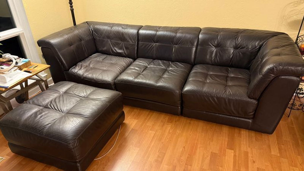 1. Chateau d’Ax sectional: dark brown leather L-shaped sofa with tufted seats and ottoman on wood floor.