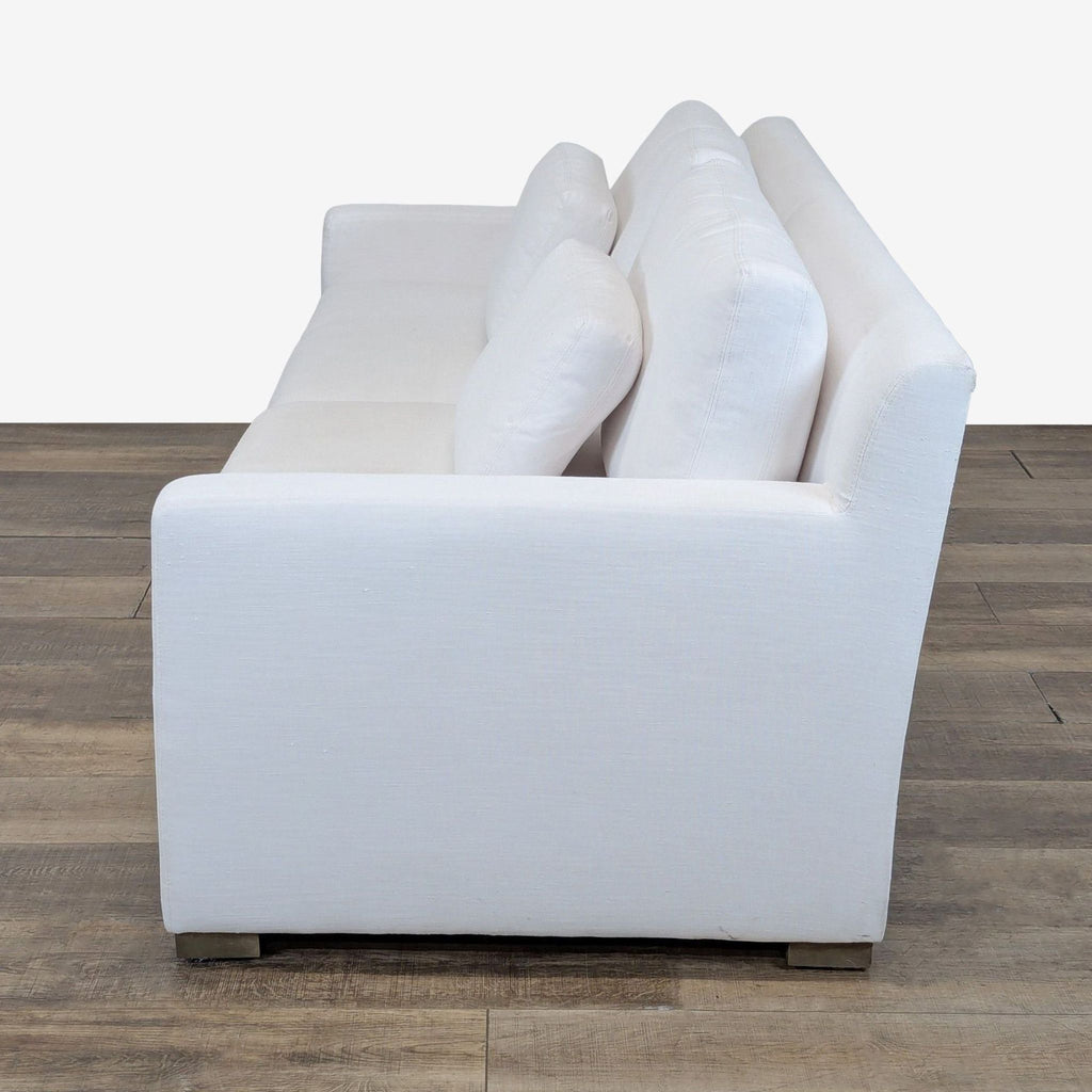 2. Side view of a white loveseat featuring deep seating, track arms, and plush cushions on wood block feet.