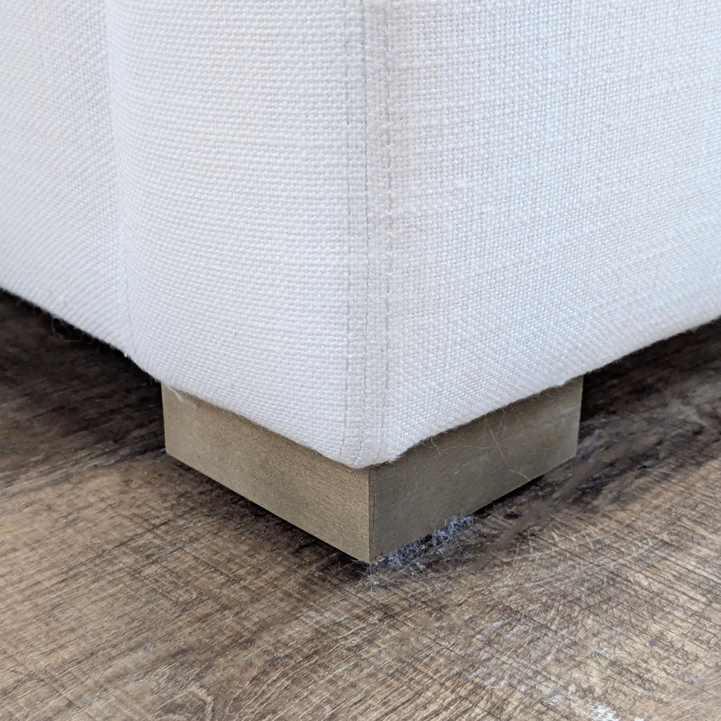 3. Close-up of the wood block foot on a white Restoration Hardware loveseat, showing textured upholstery.