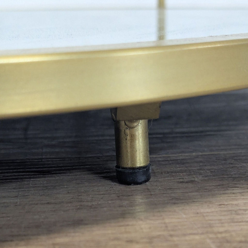 3. Detailed view of the coffee table’s gold metal leg with a black floor protector pad.