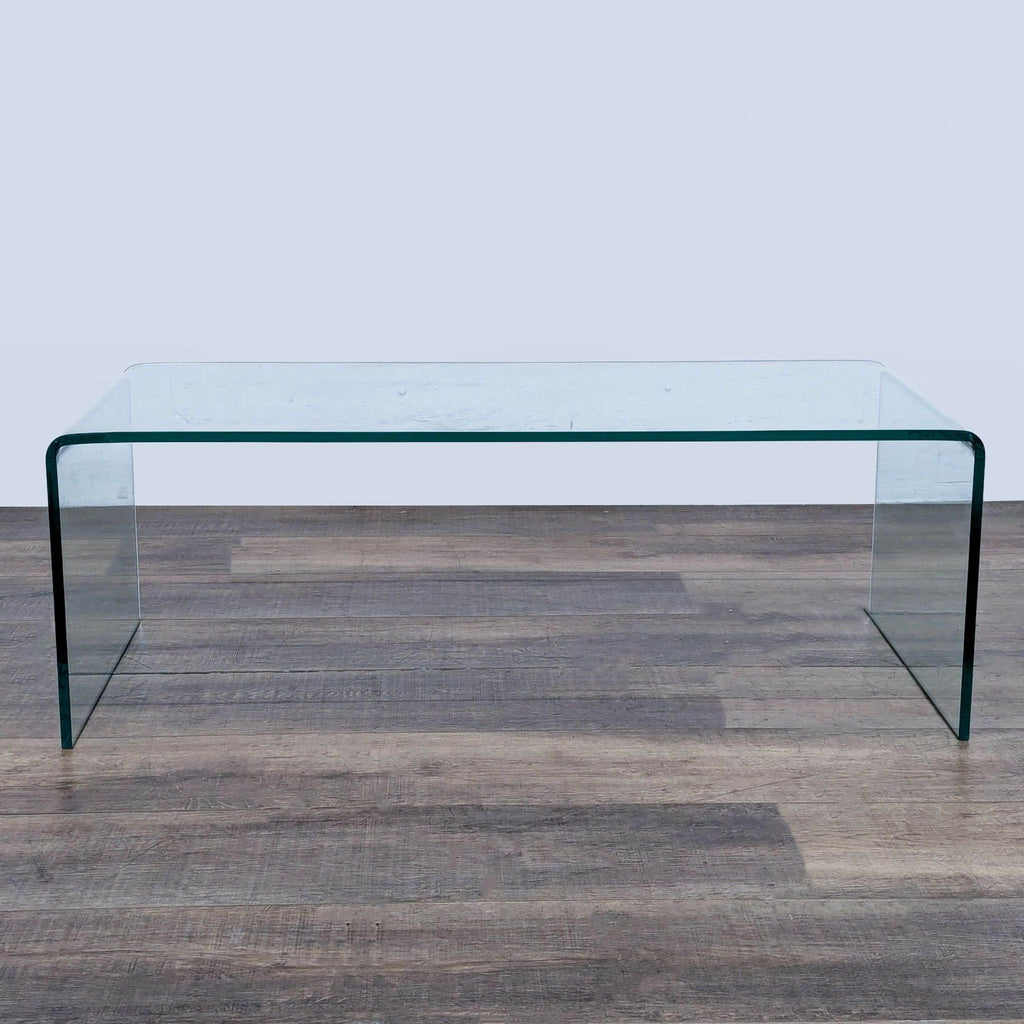 Modern glass coffee table by Ivy Bronx with a minimalist, bent rectangular design on wood flooring.