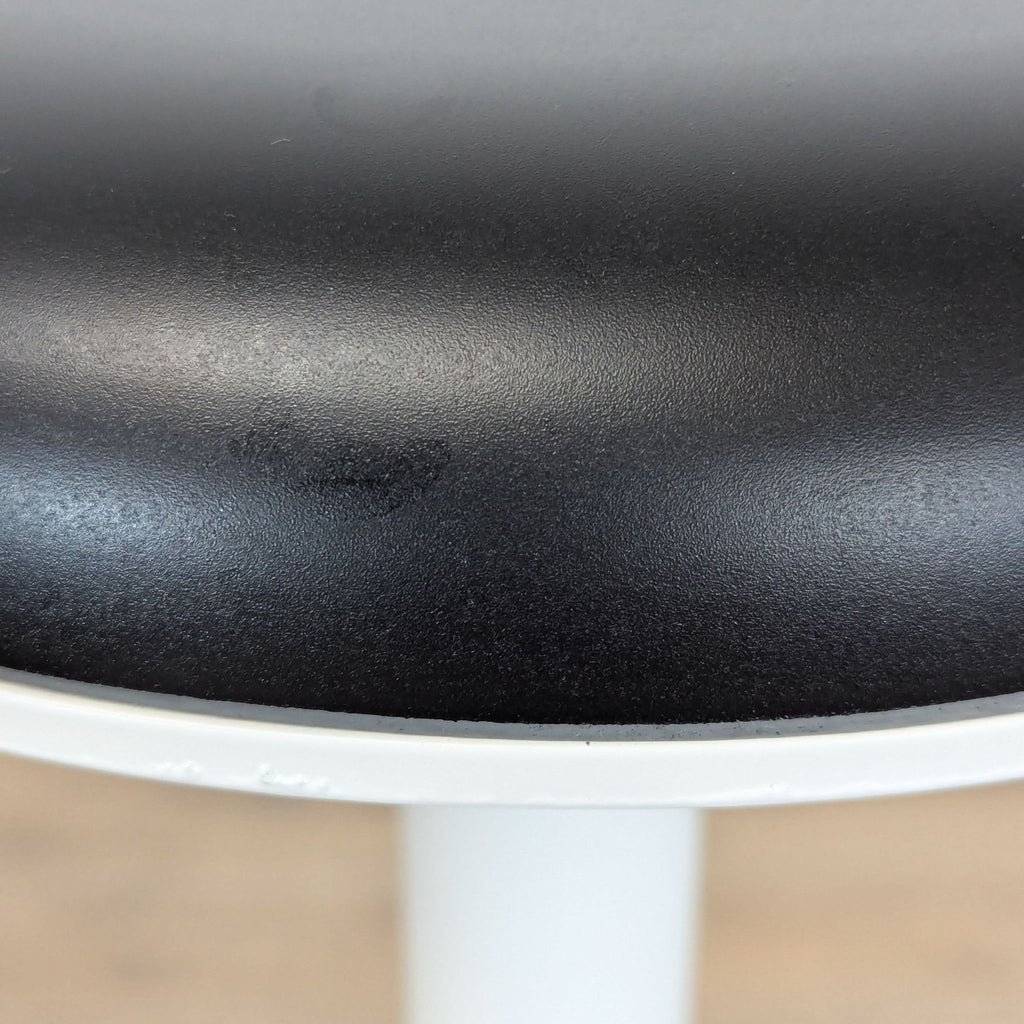 3. Detailed view of the black urethane seat surface on the Haworth Tilt Stool, showing its smooth texture.
