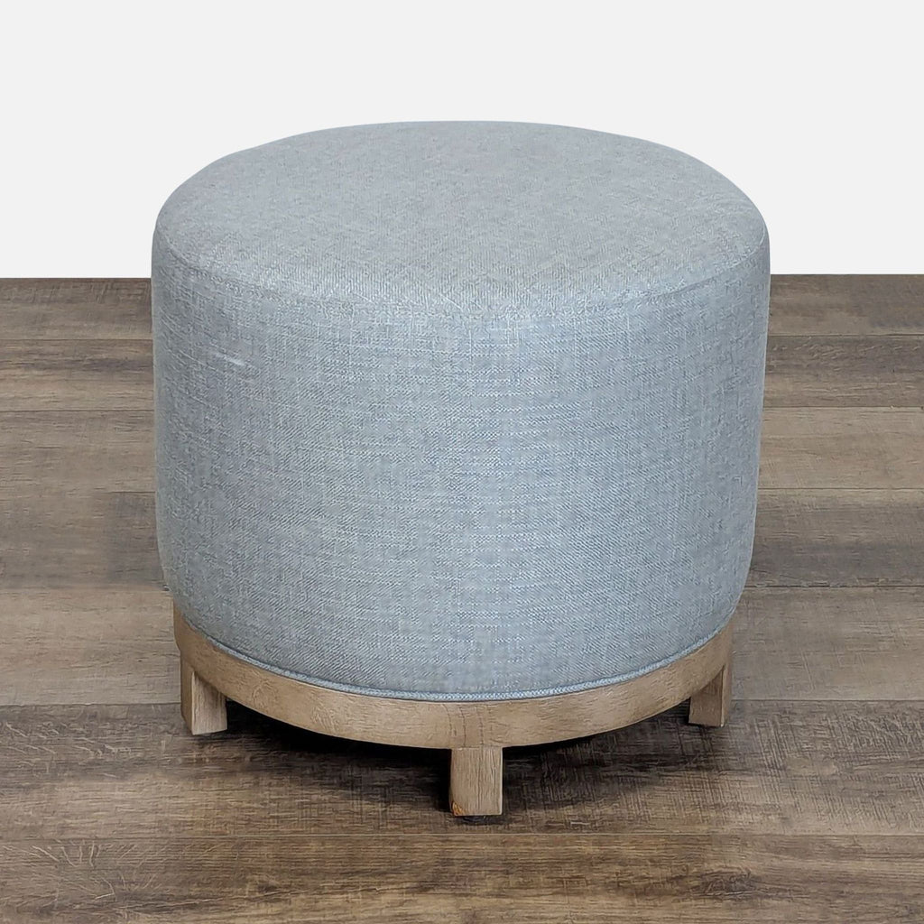 Round Pottery Barn ottoman with light grey performance basketweave upholstery and wooden base on a wood floor.