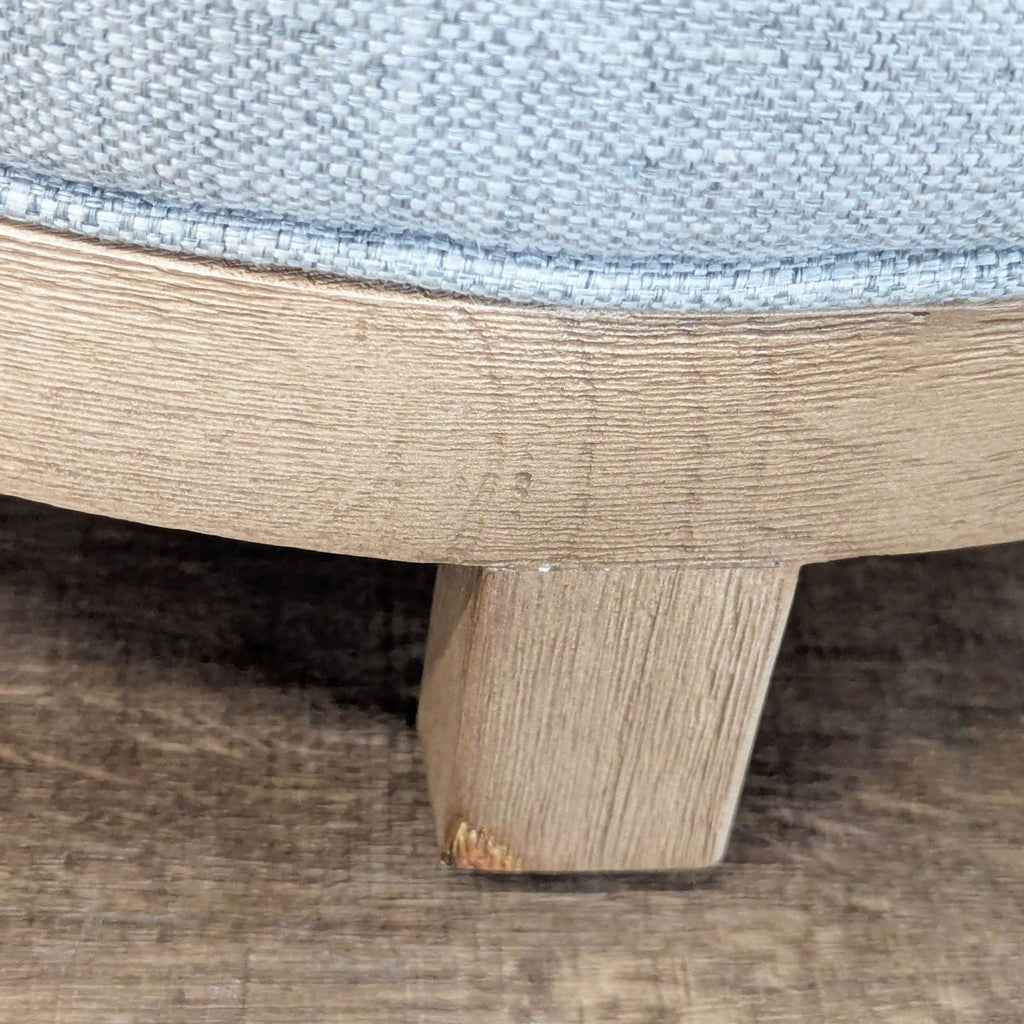 Close-up view of the Pottery Barn ottoman’s wooden leg and basketweave fabric upholstery detail.