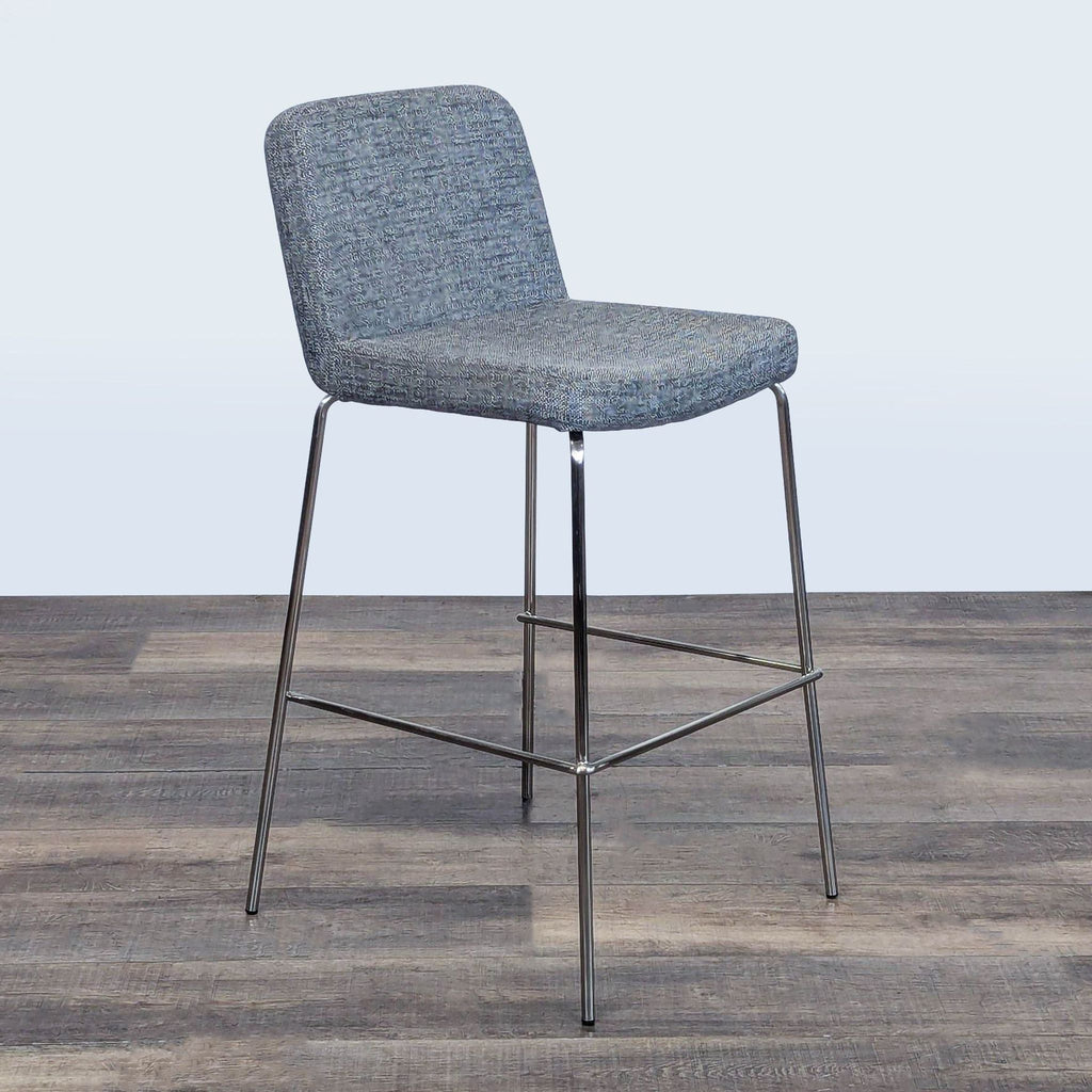 2. Angled side view of a CB2 stool, highlighting its slim chrome legs and comfy upholstered seat and backrest.