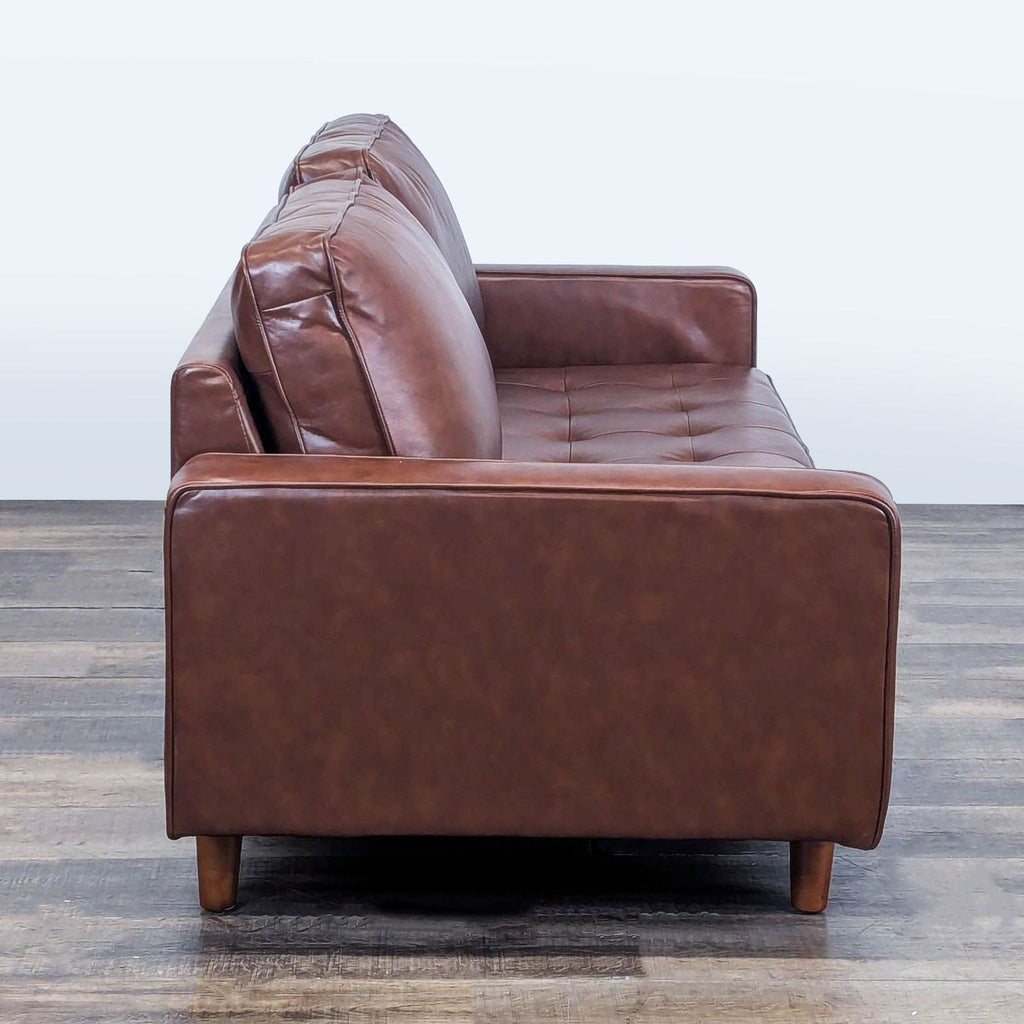 Side view of Abbyson 3-seat sofa, highlighting leather upholstery, tufted seat, and wood feet design.  