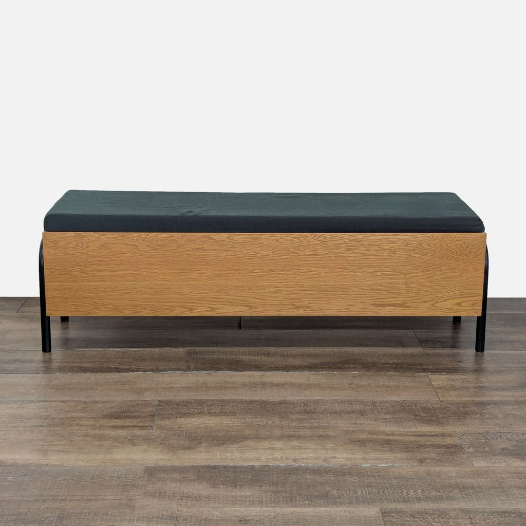 1. Rectangular CB2 bench with a black cushion and light wood base, shown on a wood floor, front view.  