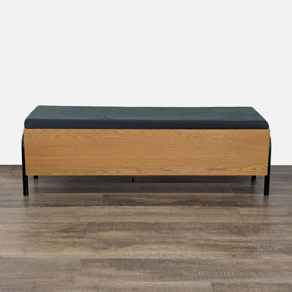 1. Rectangular CB2 bench with a black cushion and light wood base, shown on a wood floor, front view.  