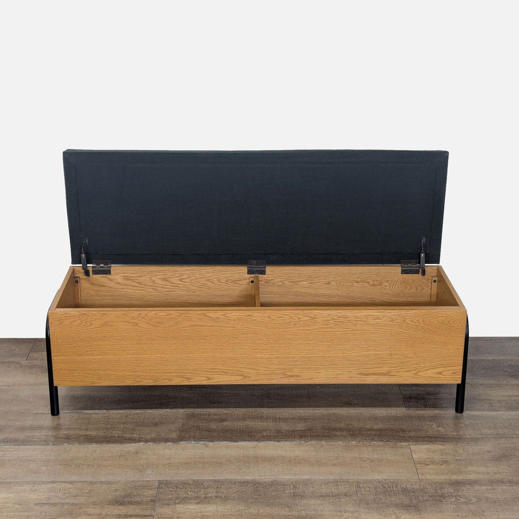 2. CB2 storage bench with black cushion, open to reveal divided interior storage, black metal legs visible.  