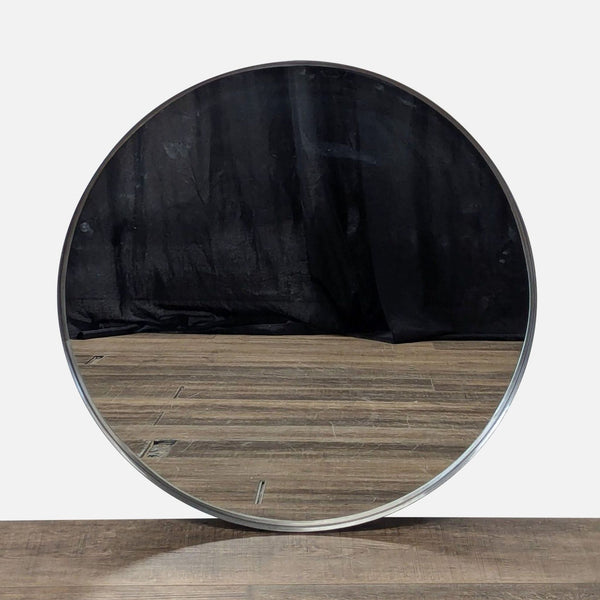 1. Round Ikea mirror with a thin, metallic frame displayed against a wooden floor and dark backdrop.  