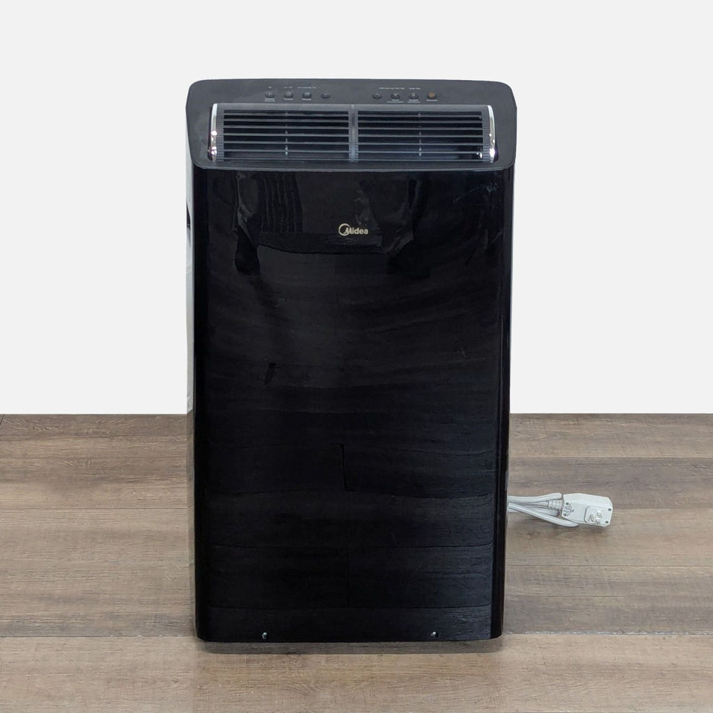 Front view of a black Midea portable air conditioner, showing control panel and air vent, on a wooden floor.