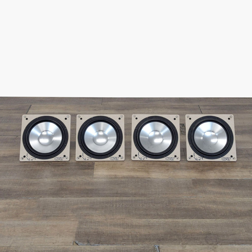 Four CAT 6.5" aluminum cone audio drivers arranged in a row on a wooden surface.
