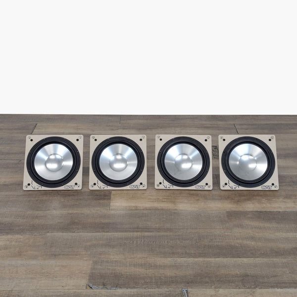 Four CAT 6.5" aluminum cone audio drivers arranged in a row on a wooden surface.