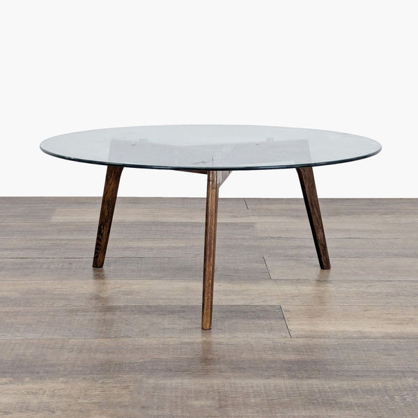 1. Article coffee table with round glass top and three angled wooden legs on a wooden floor.
