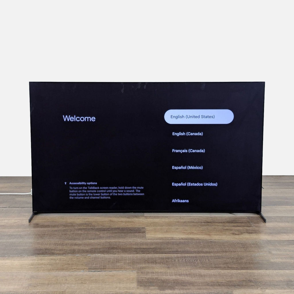 2. Sony XR-65A95L QD-OLED TV powered on, displaying a welcome screen with language options on a wooden floor.