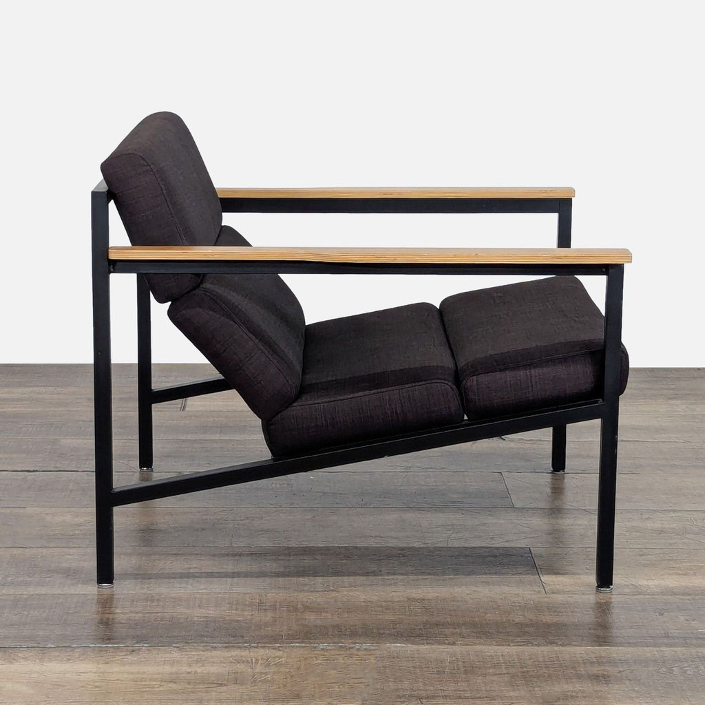 Side profile of a Gus* lounge chair highlighting its solid wood paddle armrests, faceted upholstery, and steel structure.  