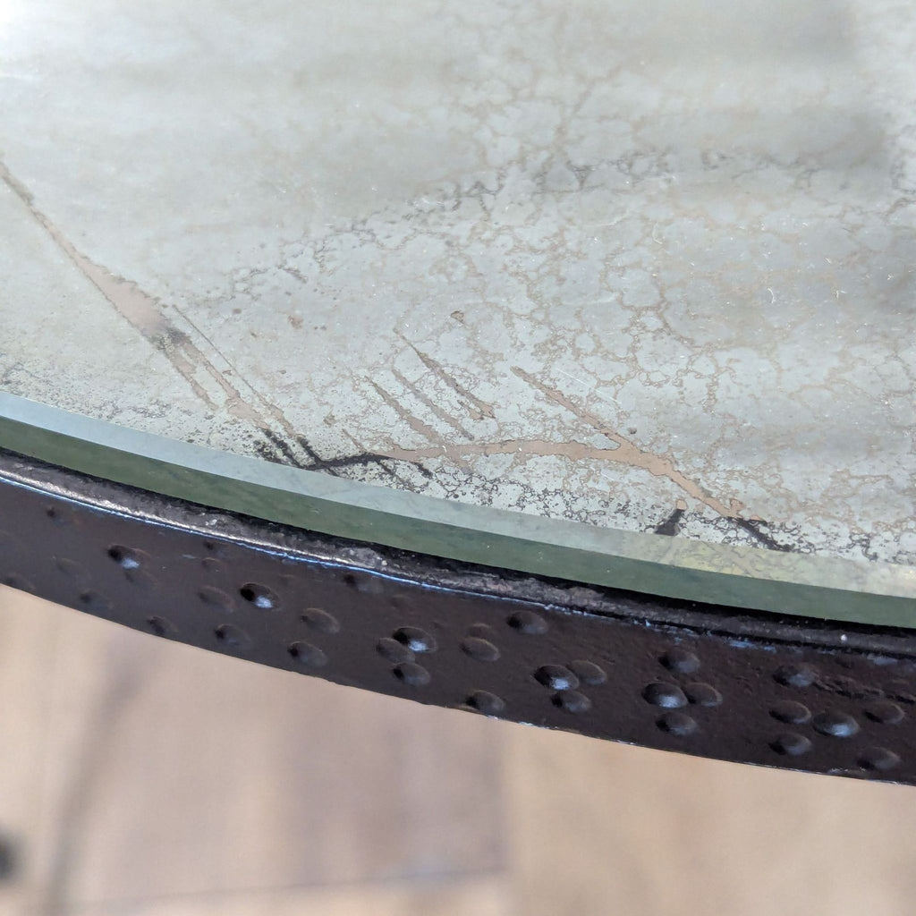 3. Close-up of the Reperch side table’s distressed glass top and hammered black metal edge detail.