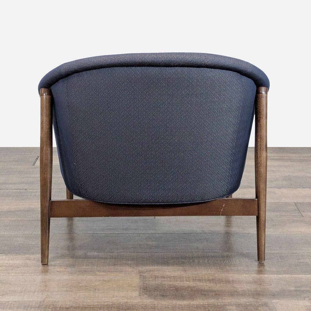 Rear view of a Reperch lounge armchair, highlighting the curved blue fabric back and wooden legs.