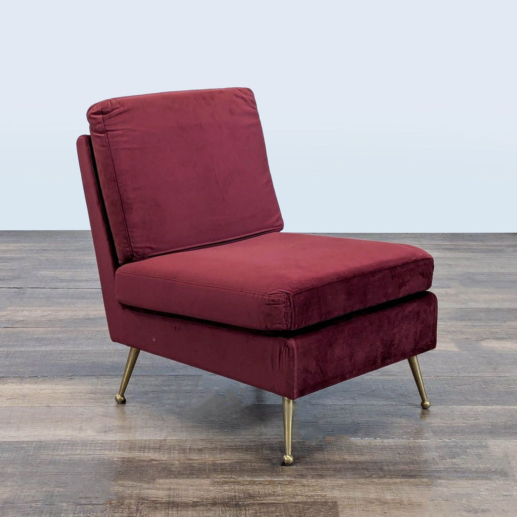 Angled view of an MXM lounge chair featuring garnet velvet fabric and modern gold tone legs.